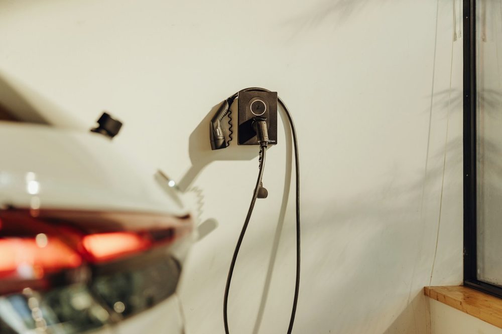 Wallbox na zdi garáže, kabel svinutý vedle, před ním zaparkované auto